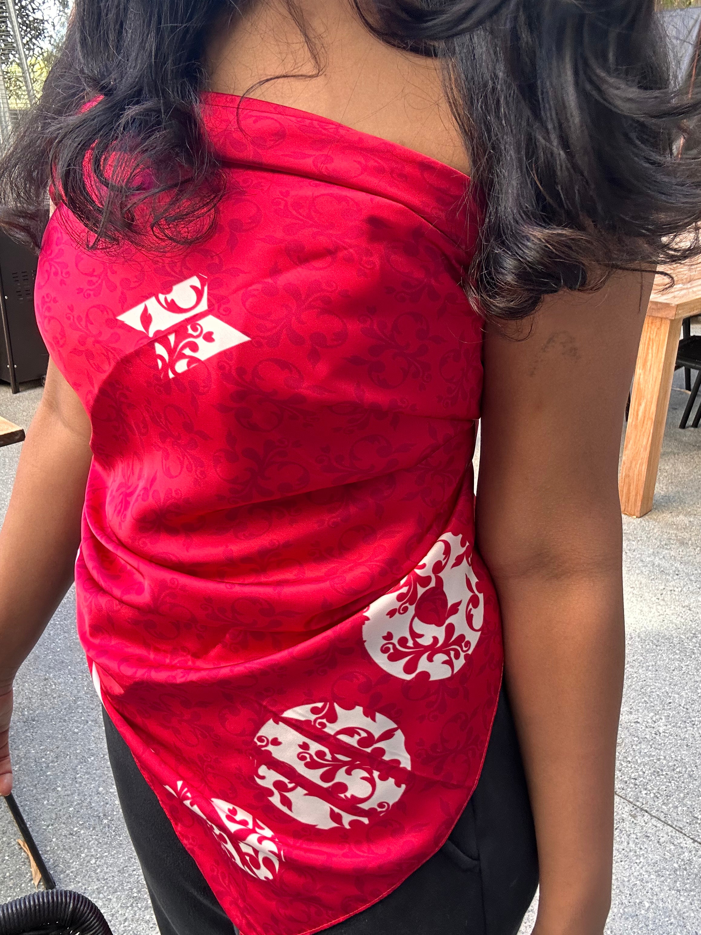 A close-up of a person wearing a bright red scarf top with white decorative printed motifs, paired with black bottoms. 