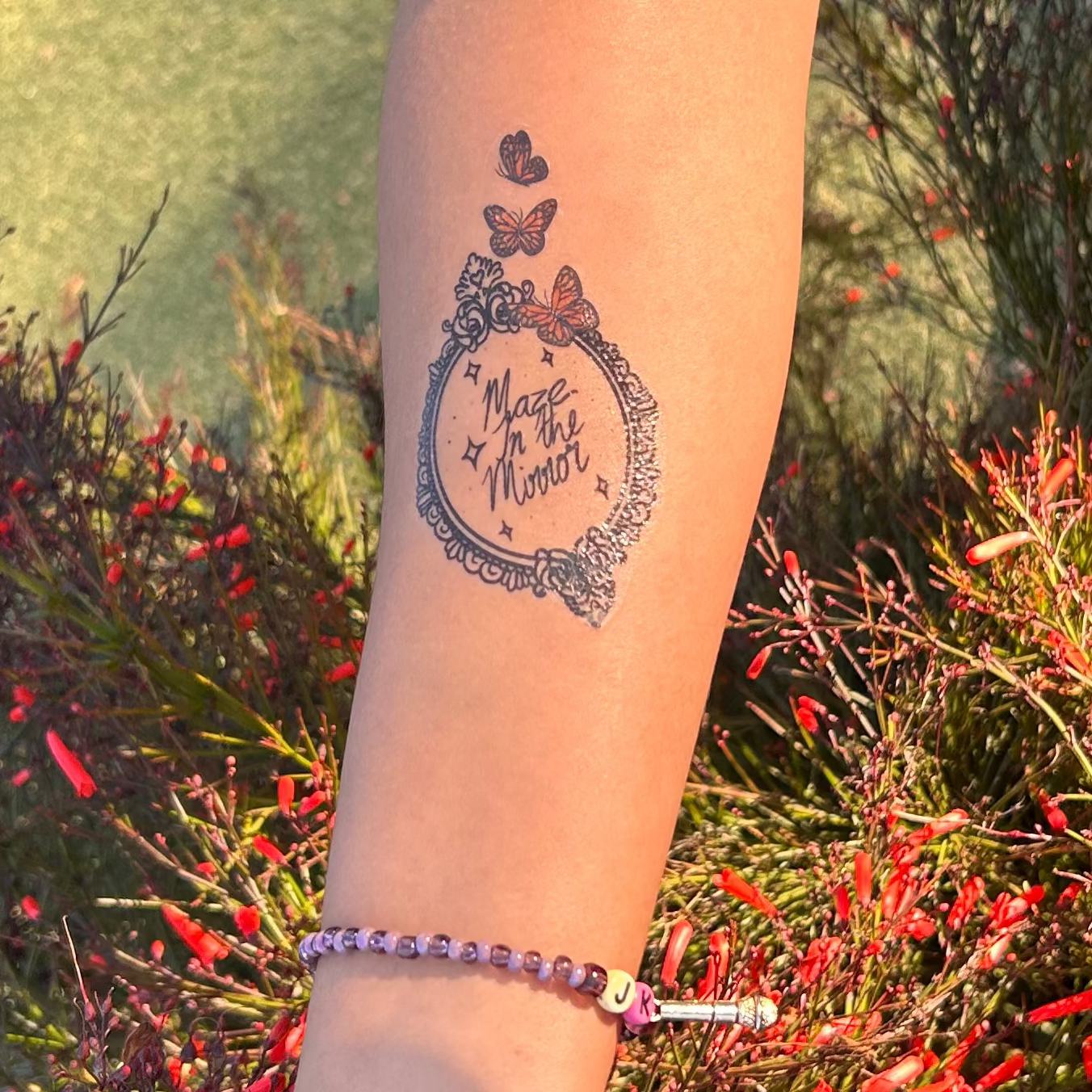 Person's arm with a tattoo in front of red flowers