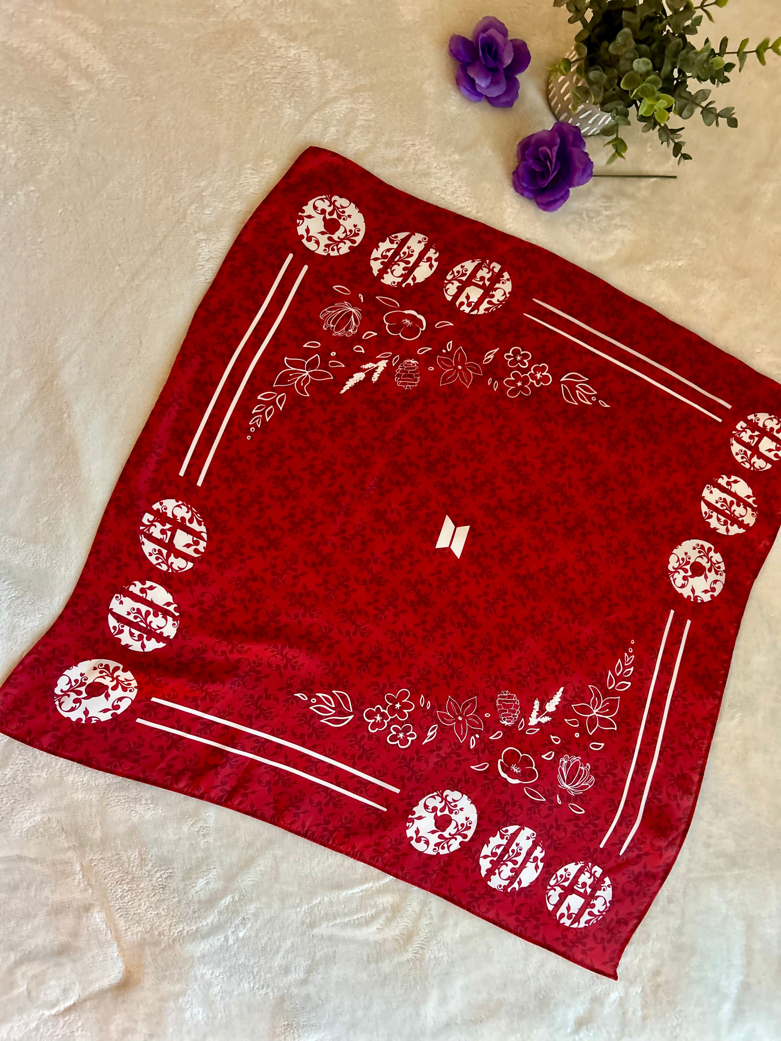 Red bandana with white patterns on a beige surface with purple flowers.
